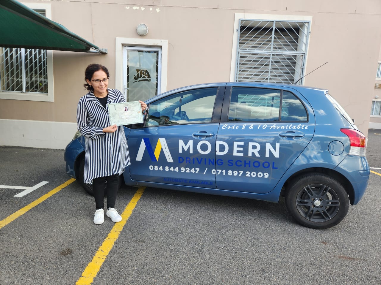 Student holding her licence next to a Modern Driving School Code 8 automatic car